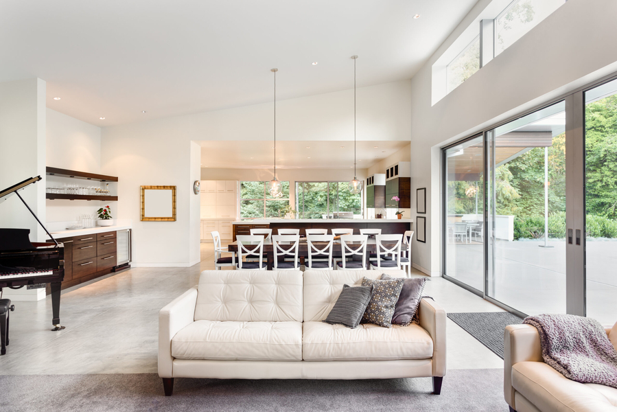A living room with white couce and a kitchen with tables and chair