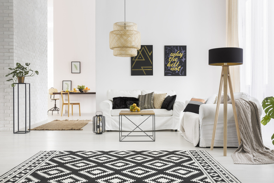 A living room with white couch and black pillows, a black and white carpet, and white walls